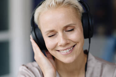 Close-up of businesswoman with eyes closed listening music over headphones in office - KNSF08656