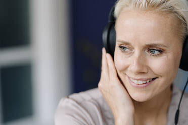 Close-up of thoughtful female entrepreneur listening music over headphones looking away in office - KNSF08657