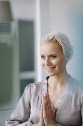 Nahaufnahme einer lächelnden Geschäftsfrau, die beim Meditieren im Büro wegschaut - KNSF08679