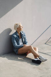 Mid adult woman with short hair sitting on flooring against wall - KNSF08681