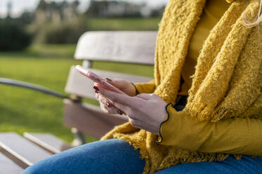 Young woman texting through smart phone while sitting on bench in park - AFVF07237