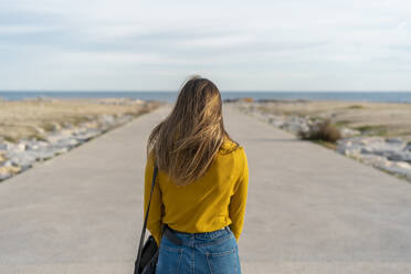 Woman with bag standing on footpath leading to sea - AFVF07242