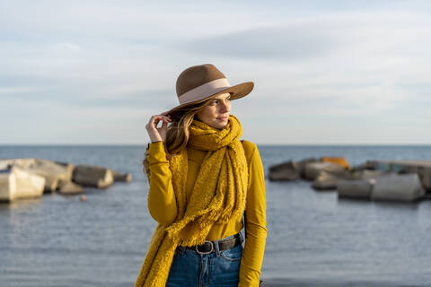 Thoughtful woman wearing sun hat while looking away against sea stock photo