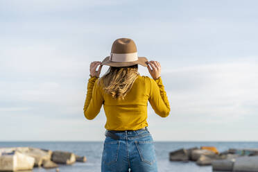 Young woman wearing sun hat while standing against sea - AFVF07248