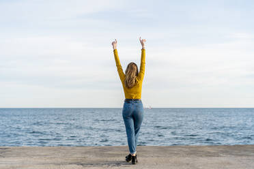 Junge Frau mit erhobenen Armen am Meer stehend - AFVF07258