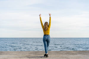 Junge Frau mit erhobenen Armen am Meer stehend - AFVF07258