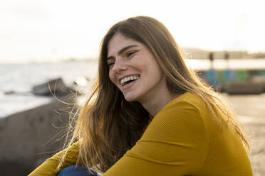 Cheerful young woman sitting by sea against sky - AFVF07263