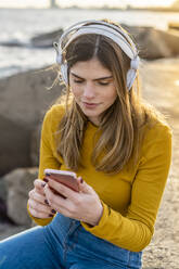 Thoughtful woman with mobile phone listening to music in city - AFVF07266