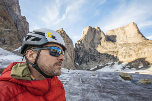 Portrait of climber wearing helmet and sunglasses below mountain summi - CAVF88782