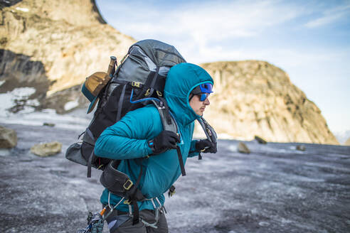 Bergsteiger hebt bei Gletscherüberquerung schweren Rucksack auf die Schultern - CAVF88788