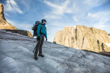 Backpacker standing on glacier below mountain summit. - CAVF88797