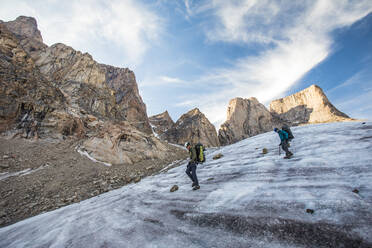 Two mountain climbers traverse a glacier below Mount Asgard. - CAVF88799