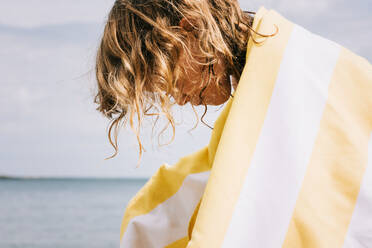 Junges Mädchen mit lockigem Haar, eingewickelt in ein gestreiftes Handtuch, am Strand - CAVF88824