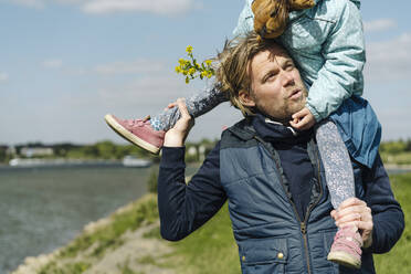 Daughter sitting on father's shoulder near Rhine river - GUSF04438