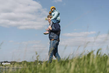 Vater geht spazieren und trägt seine Tochter auf der Schulter gegen den Himmel - GUSF04439