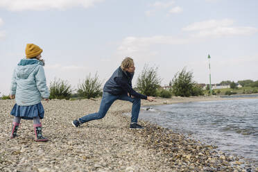 Tochter schaut zu, während der Vater einen Kieselstein in der Nähe des Flussufers ins Wasser wirft - GUSF04447