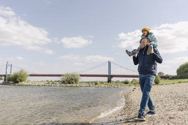 Vater, der seine Tochter auf der Schulter trägt, während er am Flussufer steht - GUSF04454