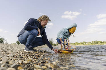 Vater und Tochter spielen mit einem Spielzeugboot in der Nähe eines Flusses - GUSF04458