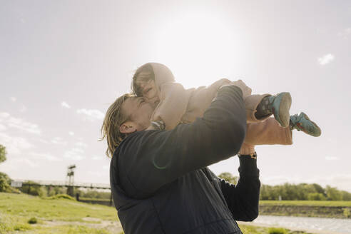 Fröhlicher Vater kuschelt mit seiner Tochter und hebt sie an einem sonnigen Tag in die Luft - GUSF04466