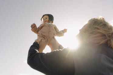 Vater trägt Tochter an einem sonnigen Tag gegen den klaren Himmel - GUSF04468