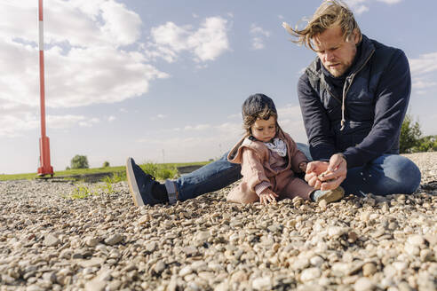 Vater und Tochter spielen mit Kieselsteinen an einem sonnigen Tag - GUSF04472