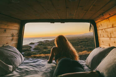 Young woman looking out to ocean from bed of camper van in Mexico. - CAVF88852