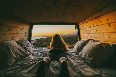 Young woman looking out to ocean from bed of camper van in Mexico. - CAVF88853