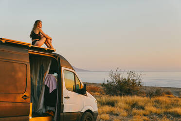 Young woman on camper van looking out to the sunrise in Baja, Mexico. - CAVF88862