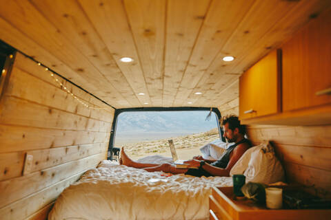 Young man on bed with laptop in camper van in northern California. stock photo