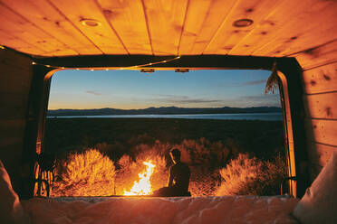 Young man by campfire in Mono Lake at night in northern California. - CAVF88875