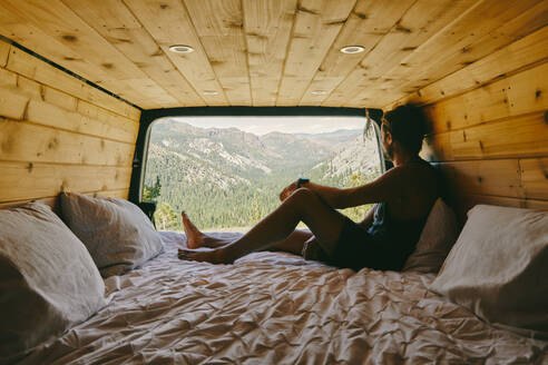 Junger Mann auf dem Bett eines Wohnmobils mit Blick auf den Yosemite Park. - CAVF88876