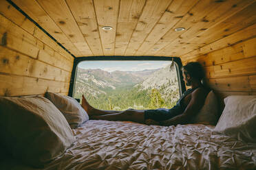 Young man sitting on bed of camper van observing the views of Yosemite - CAVF88877
