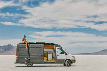 Young man sitting on roof of camper van in Bonneville Salt Flats. - CAVF88898