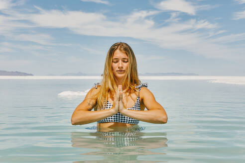 Junge Frau meditiert im Wasser in den Bonneville Salt Flats. - CAVF88901