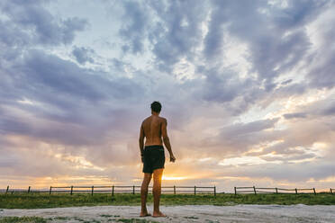 Young man standing in bathing suit against sunset in Meadow Hot spring - CAVF88903
