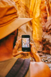 Young man wearing hat taking picture of slot canyons in Kanarra Falls - CAVF88904