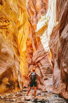 Young man wearing a hat, exploring a slot canyon in Kanarra Fall, Utah - CAVF88905