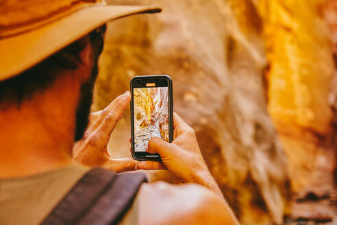 Young man wearing hat taking picture of slot canyons in Kanarra Falls - CAVF88906