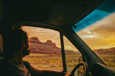 Junger Mann, der beim Fahren in der Wüste von Moab, Utah, in den Sonnenuntergang blickt. - CAVF88930
