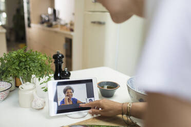 Frau führt Videochat mit Freunden auf einem digitalen Tablet-Bildschirm in der Küche - CAIF29520