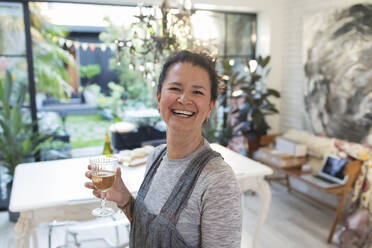 Porträt glückliche Frau trinkt Weißwein in Küche - CAIF29521