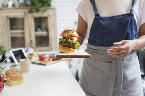 Frau serviert Hamburger auf Schneidebrett in Küche - CAIF29523