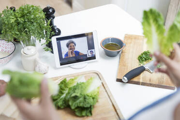 Frau mit Salat beim Kochen und Video-Chat mit Freunden in der Küche - CAIF29524