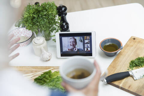 Woman drinking tea and cooking while video chatting with friends stock photo