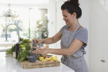 Frau beim Kochen mit Mörser und Stößel am Schneidebrett in der Küche - CAIF29537