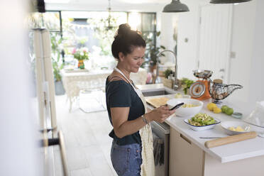 Frau mit Smartphone beim Kochen in der Küche - CAIF29539