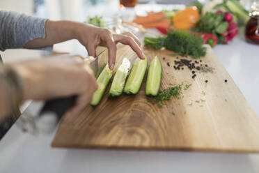 Close up woman slicing fresh cucumbers on cutting board - CAIF29541