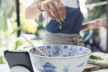 Woman sprinkling fresh herbs in bowl - CAIF29551