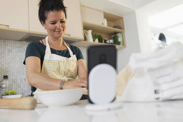 Frau mit Smartphone beim Backen in der Küche - CAIF29562