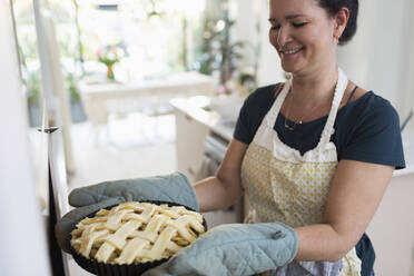 Lächelnde Frau, die einen Apfelkuchen mit Gitter in den Ofen schiebt - CAIF29566